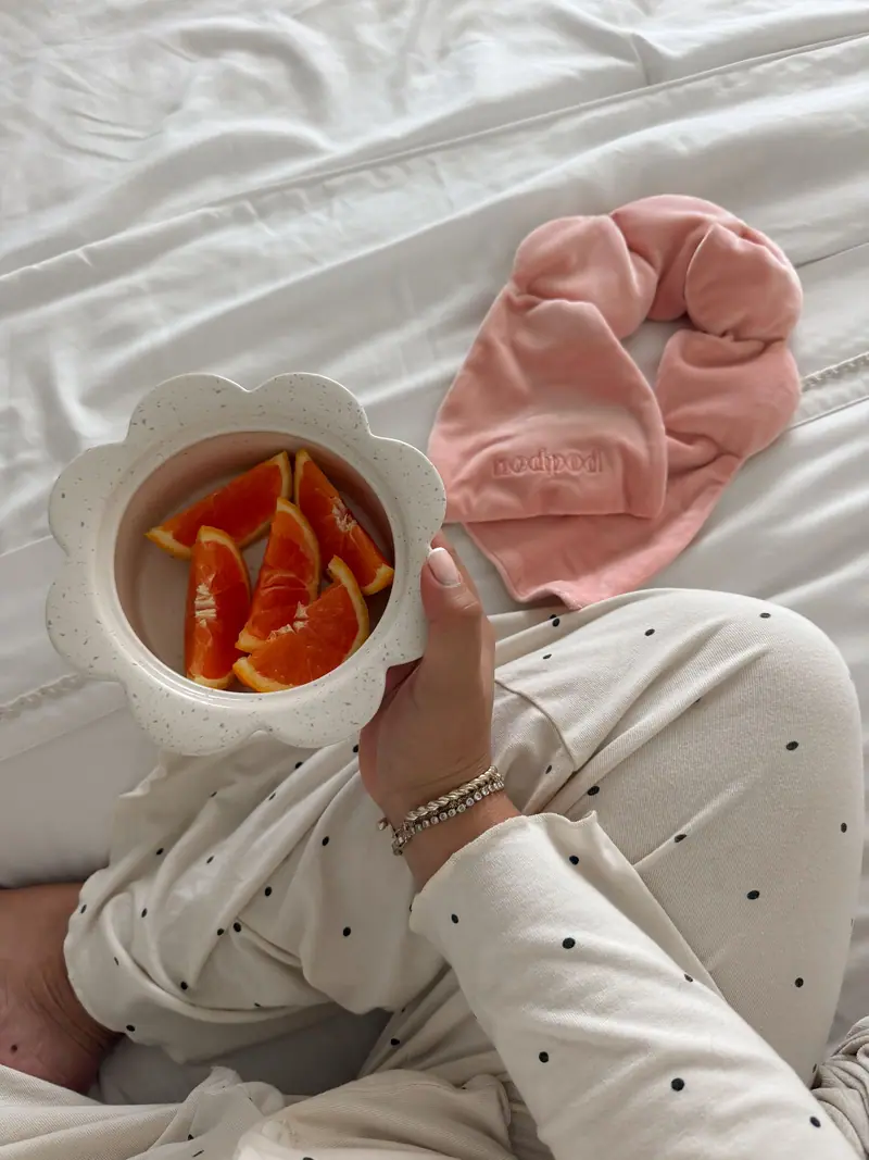 Orange slices in a scalloped bowl beside a pink velvet wrap on white bedding